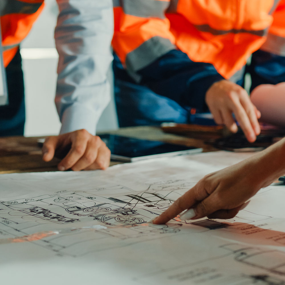 Image en plan rapproché, montrant une table avec des plans d'ingénierie et des bras pointant ces plans